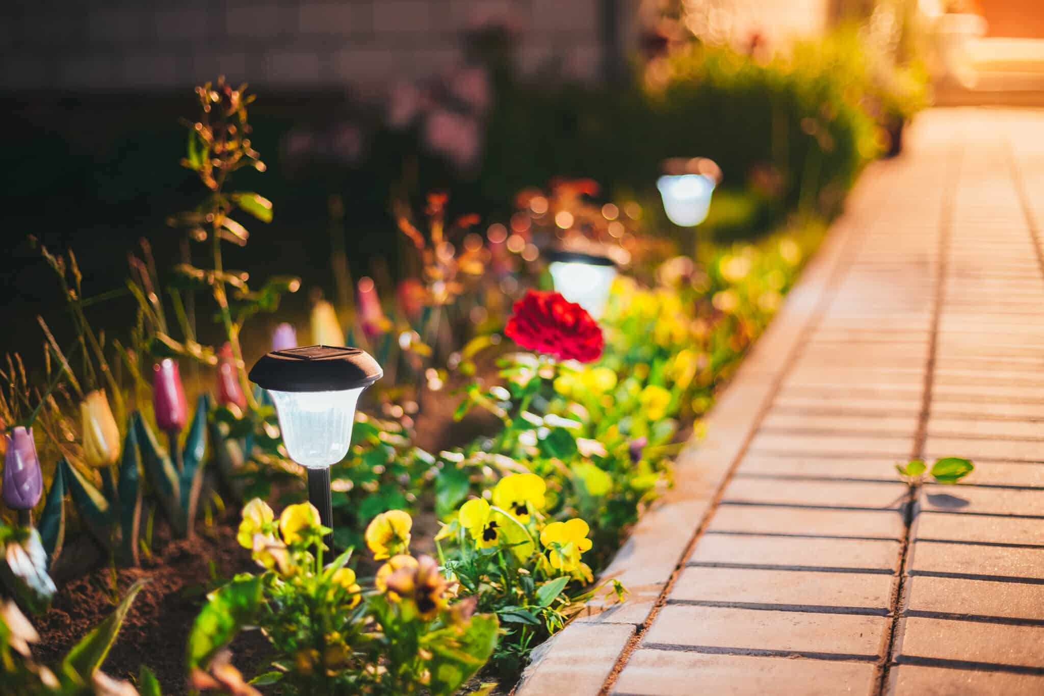 Decorative small solar powered outdoor lanterns nestled among green foliage in a flower bed, enhancing garden design.